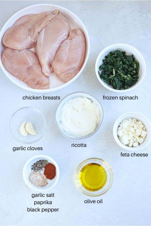 ingredients for making spinach and cheese stuffed chicken on light gray surface with captions. 