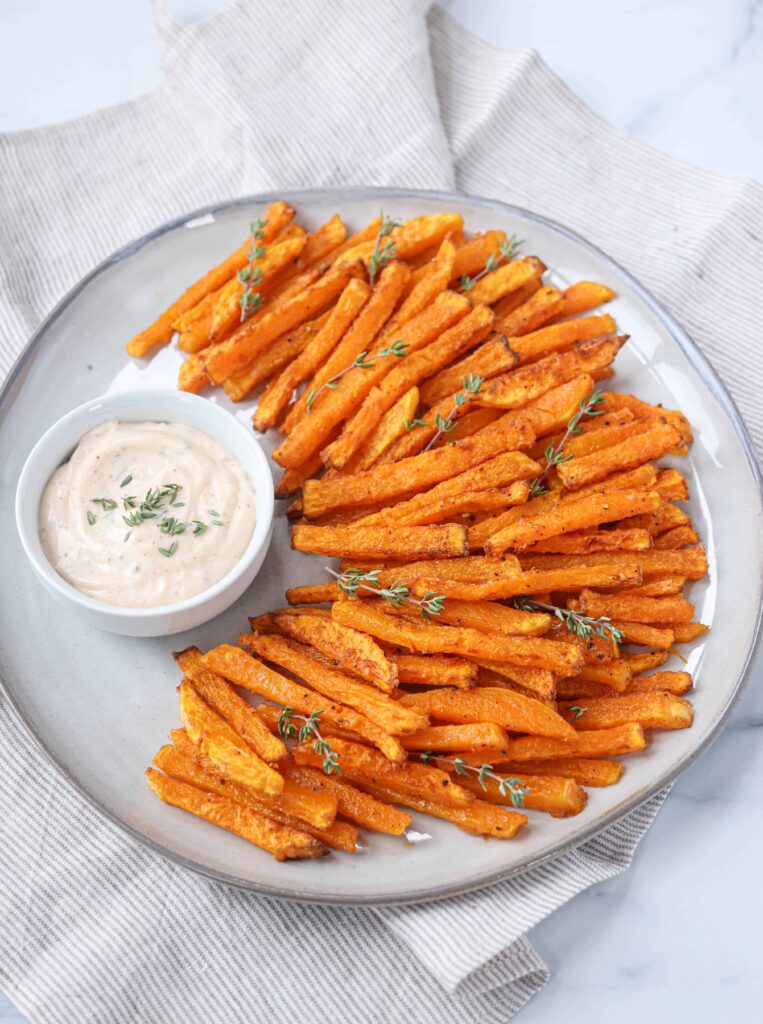 butternut squash fries made in an air fryer with a side of sauce on a large gray plate. 