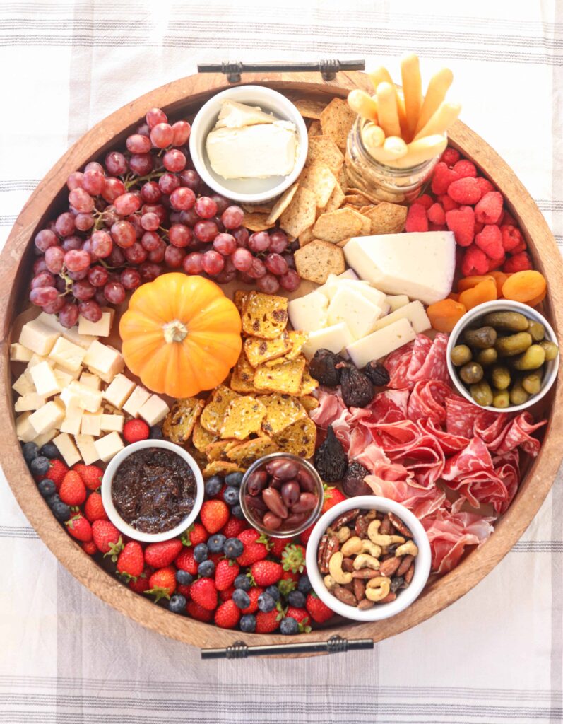 large round fall charcuterie board with cheese, fruit, cured meats, nuts and condiments. 
