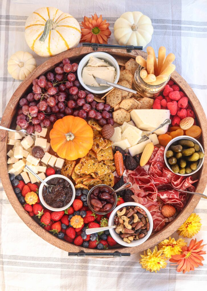 large round fall charcuterie board with cheese, fruit, cured meats, nuts and condiments. 