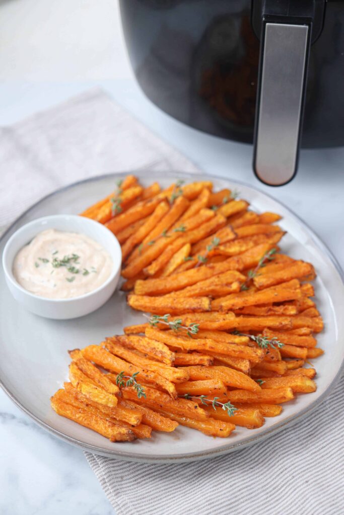 butternut squash fries made in an air fryer with a side of sauce on a large gray plate. 