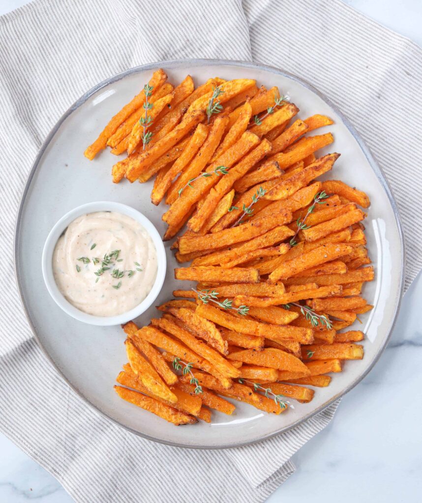 butternut squash fries made in an air fryer with a side of sauce on a large gray plate.