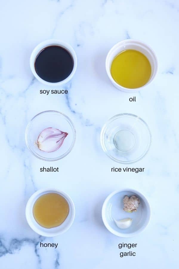 six round dishes with ginger honey dressing ingredients on white marble surface