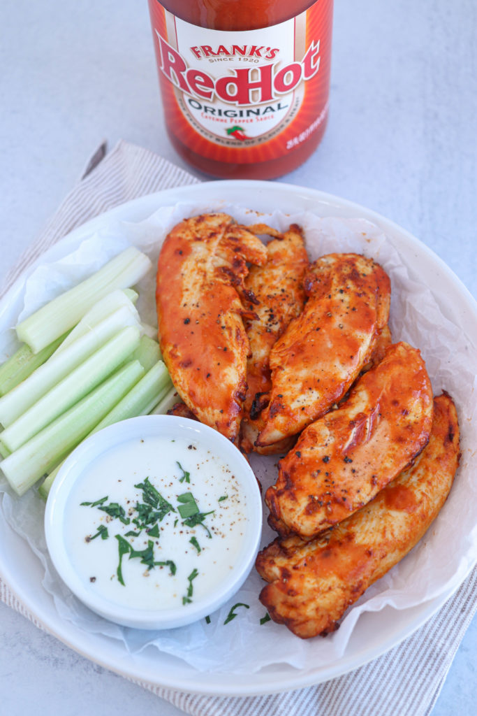air fryer buffalo chicken tenders on a white round place with a side of celery and blue cheese dressing