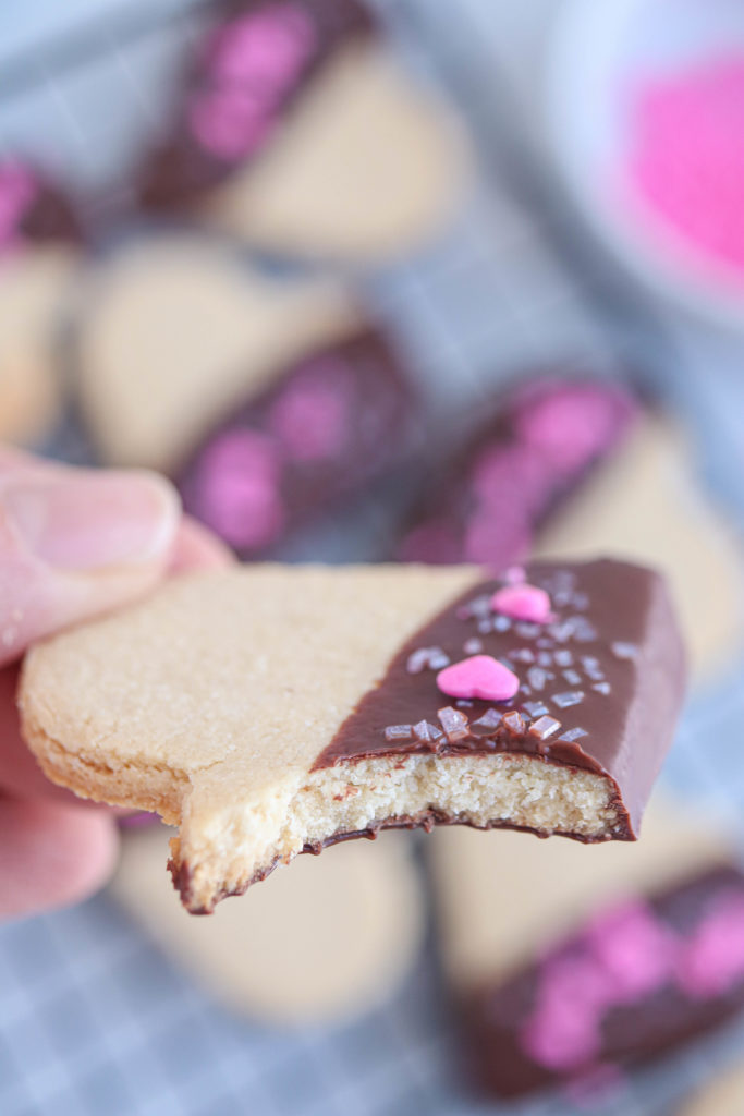 vegan heart shaped chocolate dipped cookie with a bite taken out.
