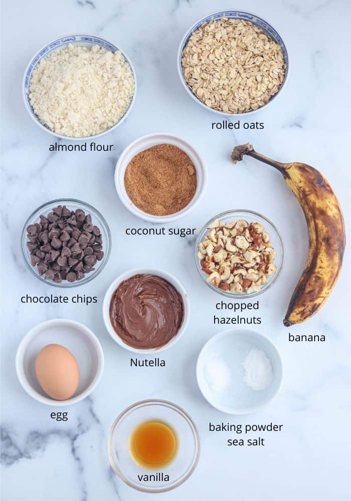 banana Nutella oatmeal cookies ingredients laid out on marble counter in round containers with captions