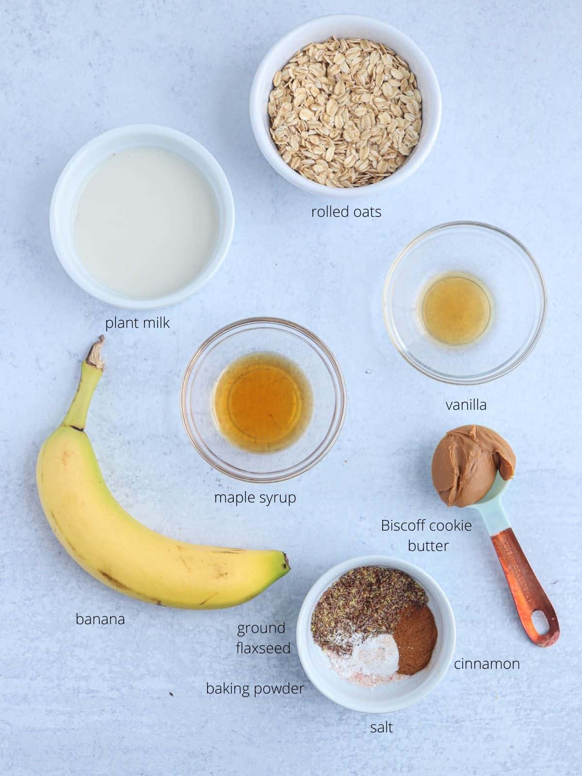 biscoff baked oats ingredients laid out on light gray surface in small round containers.
