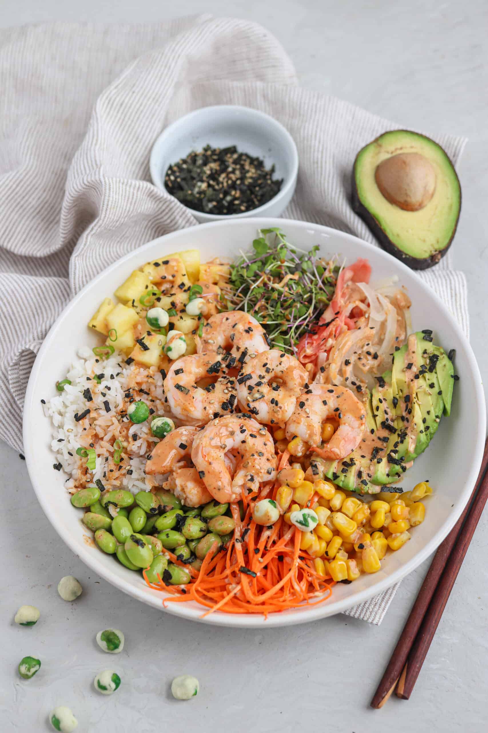 shrimp poke bowl in a white bowl with rice, pineapple, cooked shrimp, edamame, corn, carrots, microgreens and creamy spicy mayo.