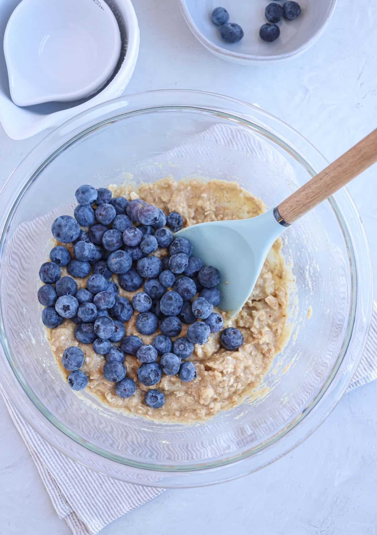 glass bowl with muffin batter and fresh blueberries added on top. 
