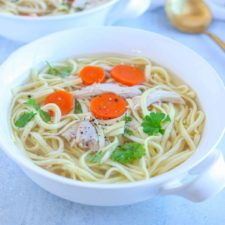 a white bowl with homemade chicken noodle soup with carrots and parsley leaves