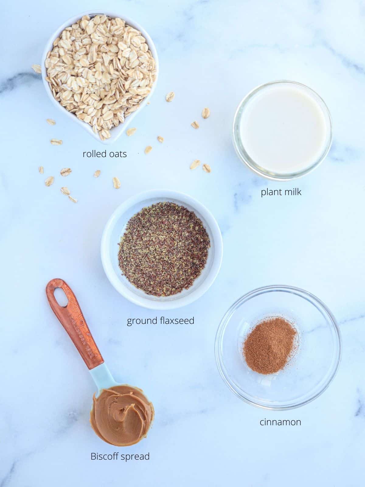 biscoff overnight oats ingredients in small containers on white marble surface.