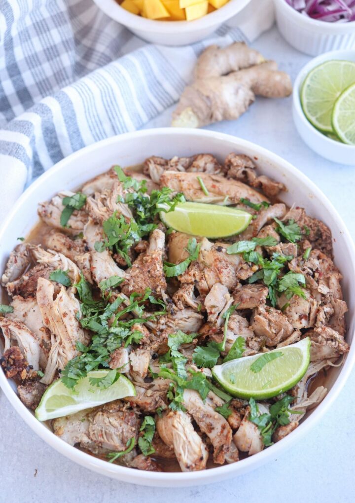 shredded jerk chicken in a white bowl with lime wedges and chopped cilantro