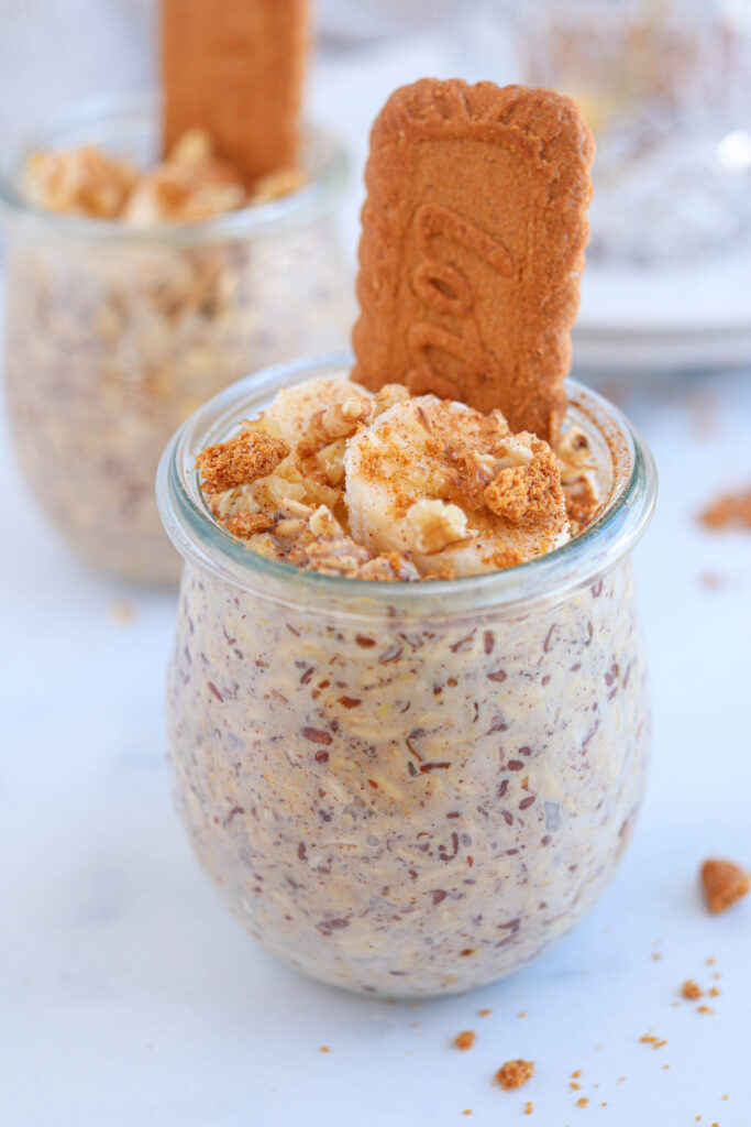 biscoff overnight oats in a tulip jar topped with sliced banana, walnuts and crushed biscoff cookies.