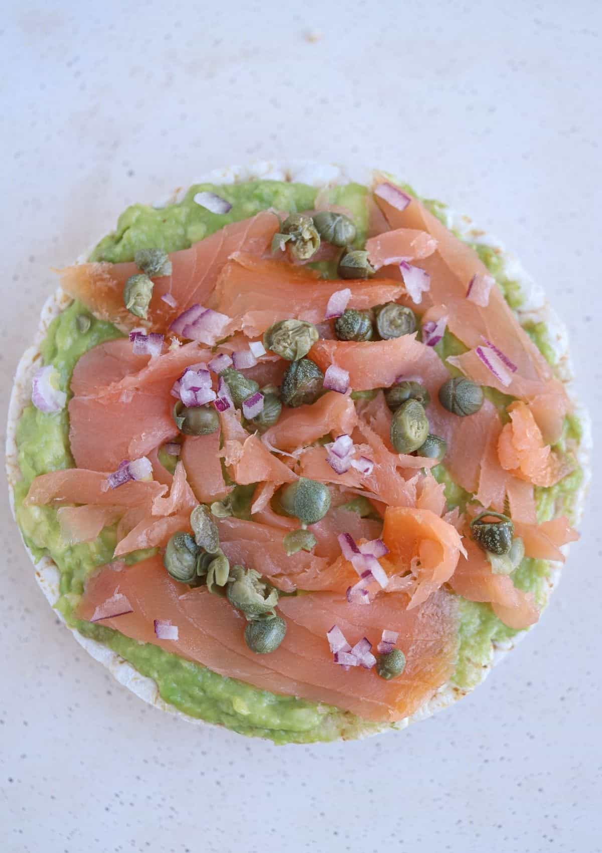 rice cake topped with mashed avocado, smoked salmon, chopped red onion and capers.