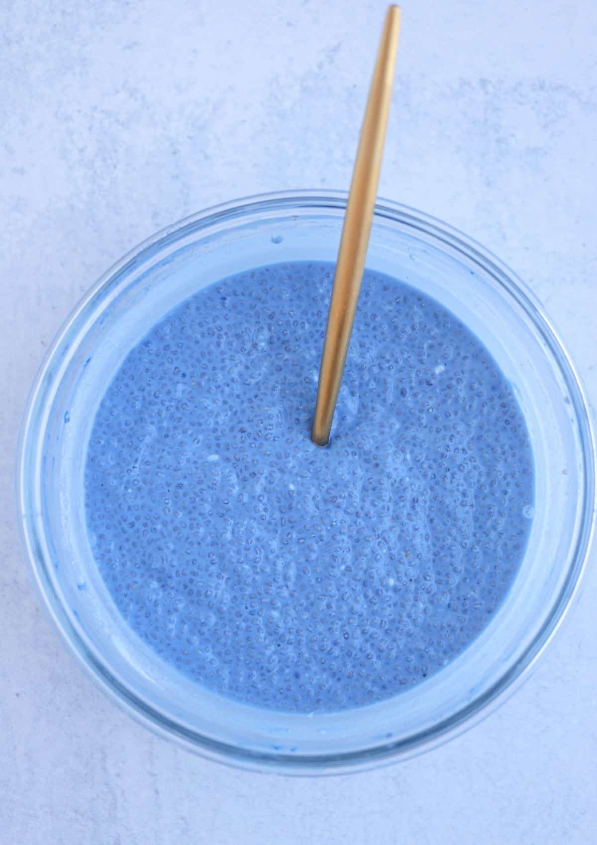 mixing blue chia pudding in a glass bowl with a golden spoon. after setting in the fridge.