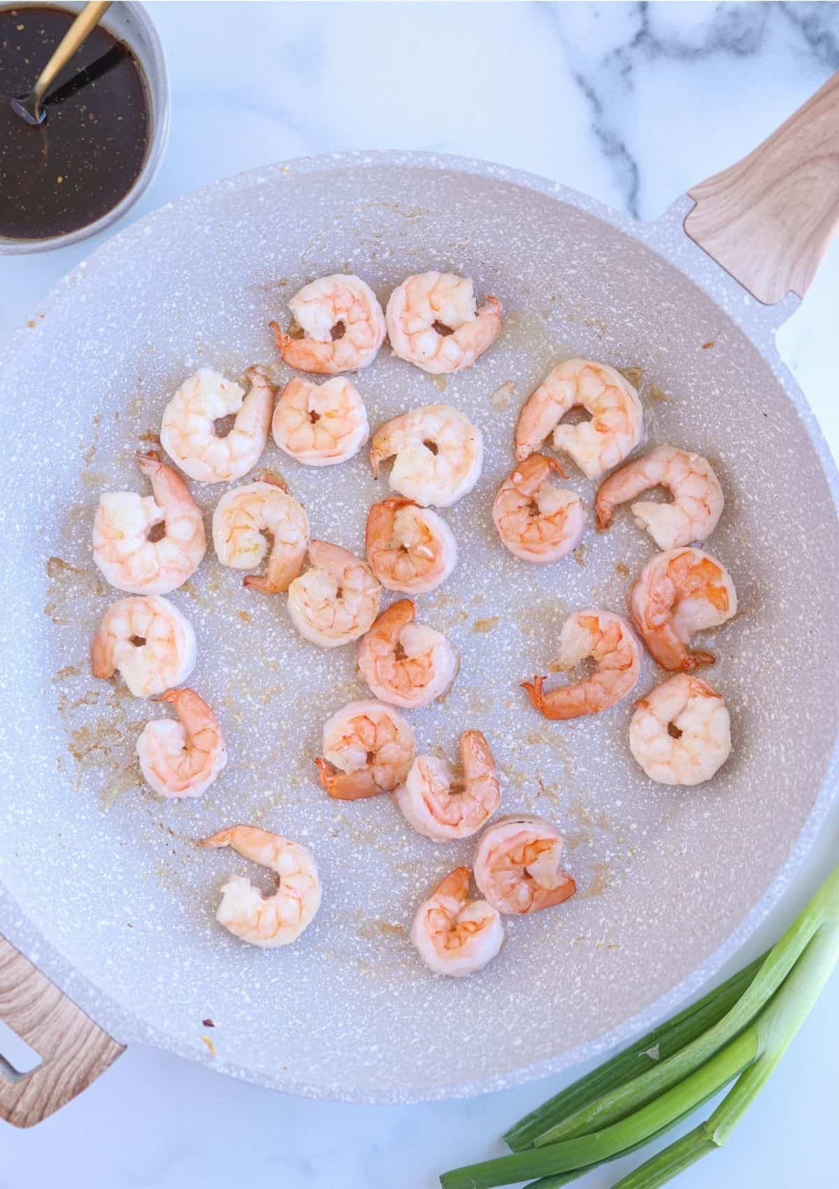 shrimp cooking in a large light grey skillet.