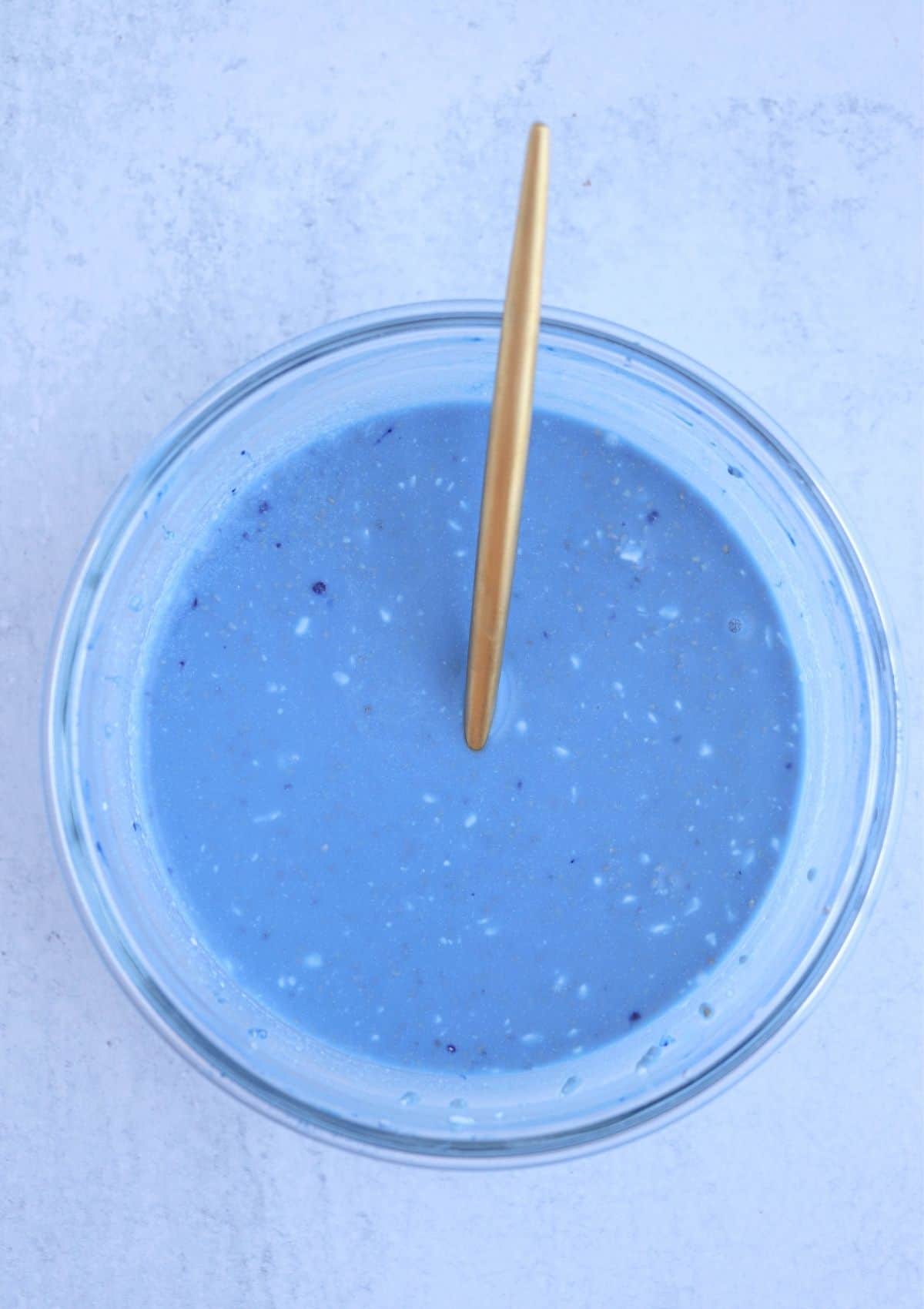 mixing blue chia pudding in a glass bowl with a golden spoon.