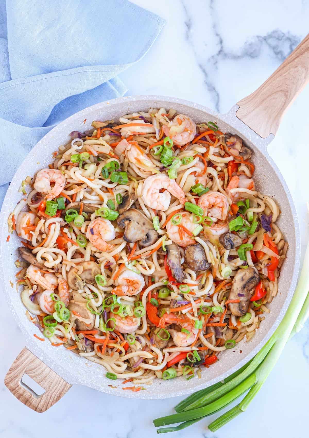 a large skillet with shrimp yaki udon noodle stir-fry with mushrooms and veggies. 