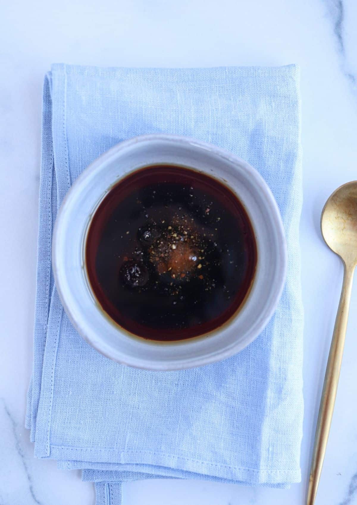 yaki udon sauce in a small grey bowl on a blue napkin with a golden spoon nearby.