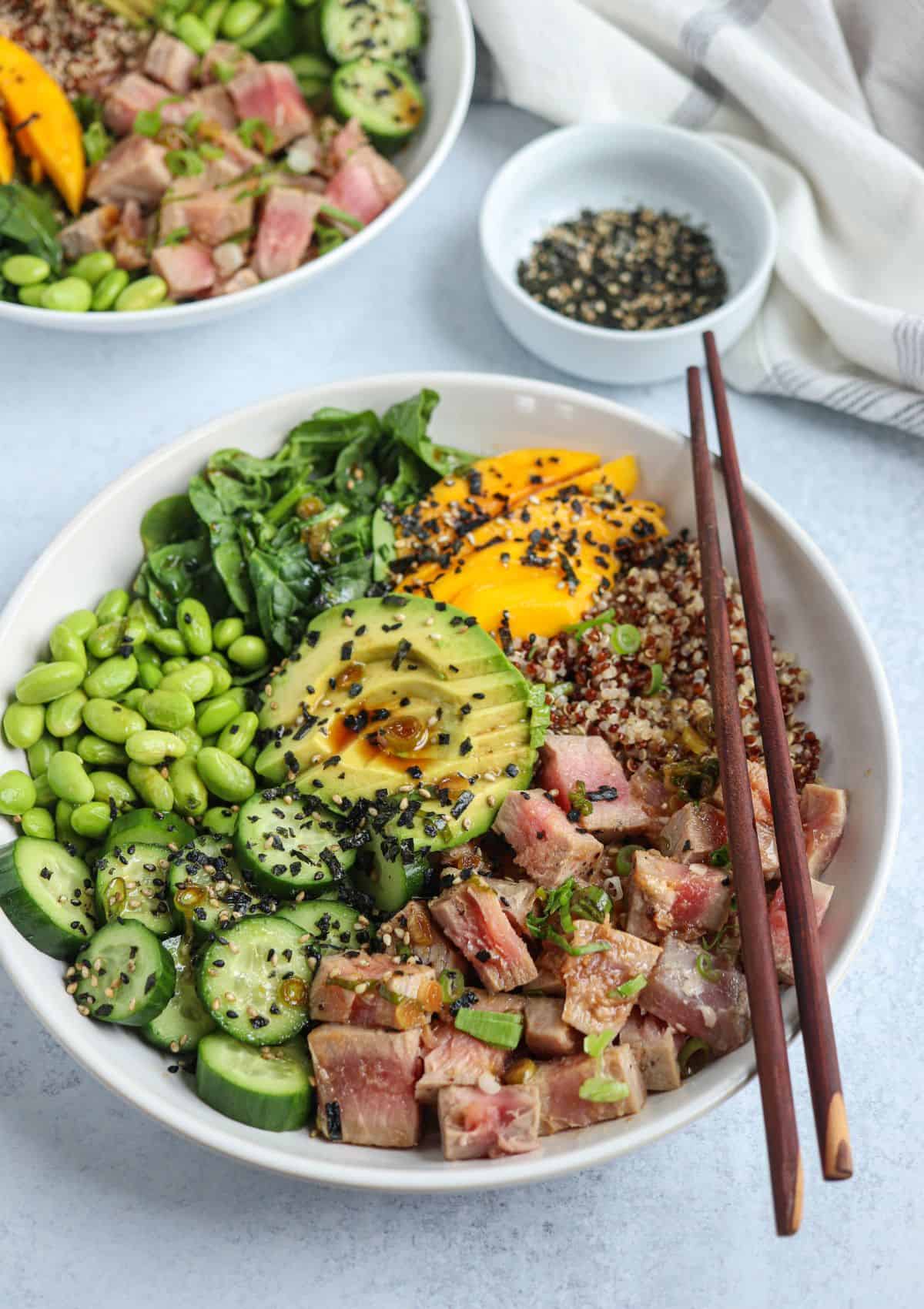 quinoa poke bowl with quinoa, seared ahi tuna, edamame, cucumber, mango, spinach and avocado sprinkled with furikake in a white bowl