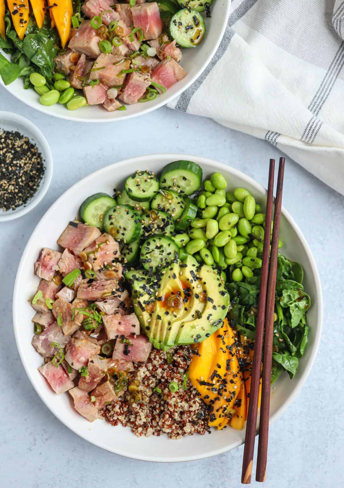 quinoa poke bowl with quinoa, seared ahi tuna, edamame, cucumber, mango, spinach and avocado sprinkled with furikake in a white bowl