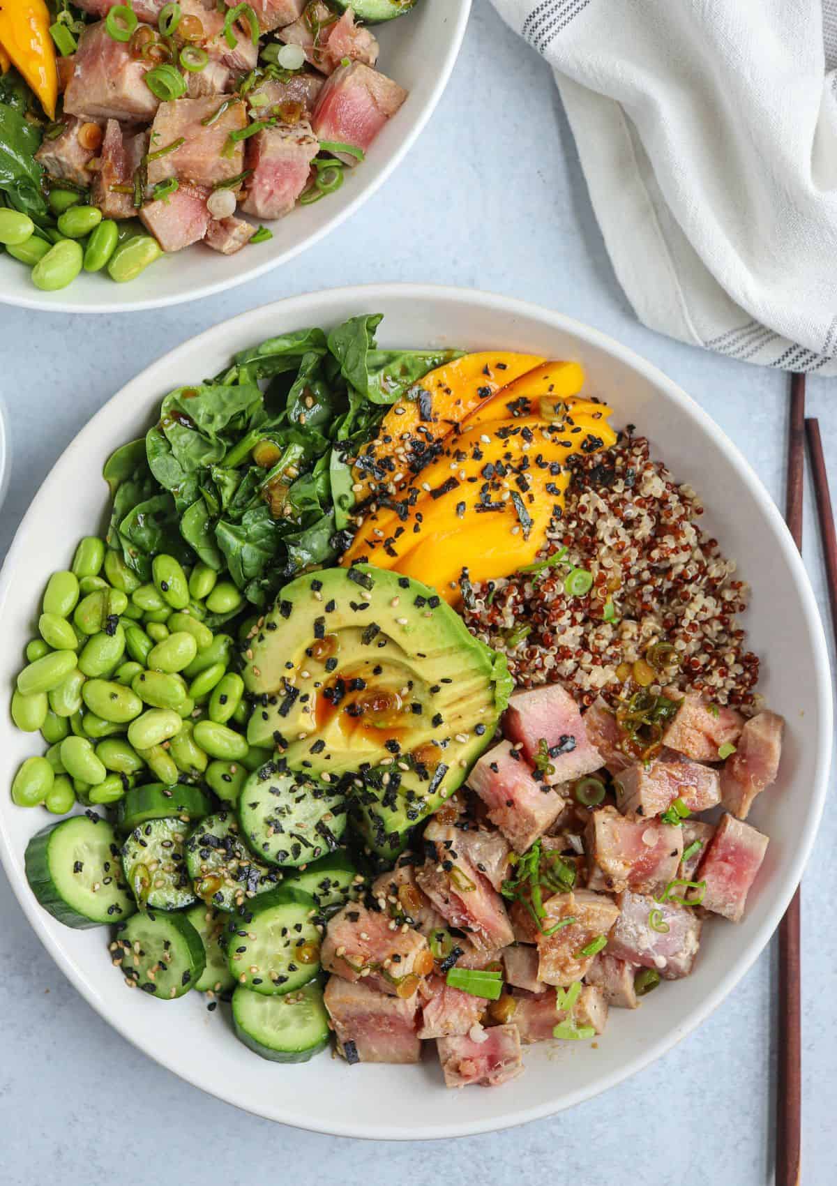 quinoa poke bowl with quinoa, seared ahi tuna, edamame, cucumber, mango, spinach and avocado sprinkled with furikake in a white bowl