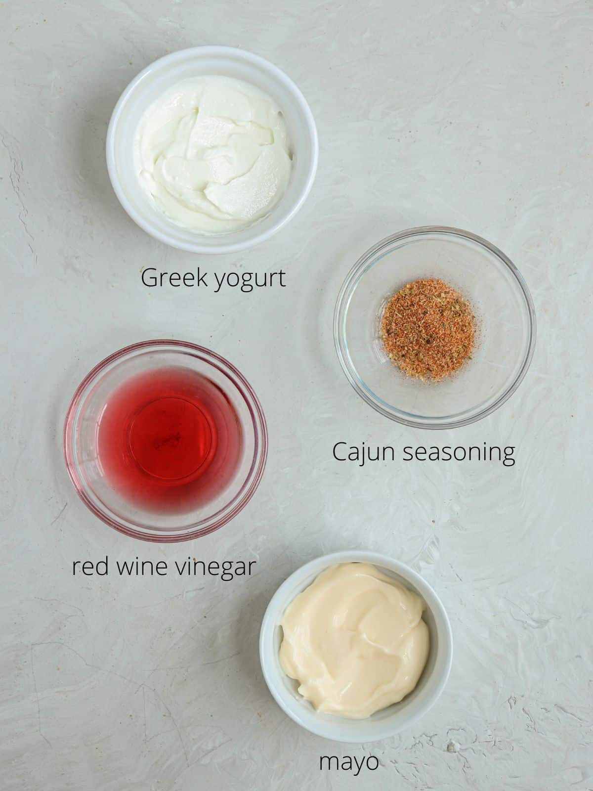 ingredients for making cajun salad dressing in round small containers on gray background.