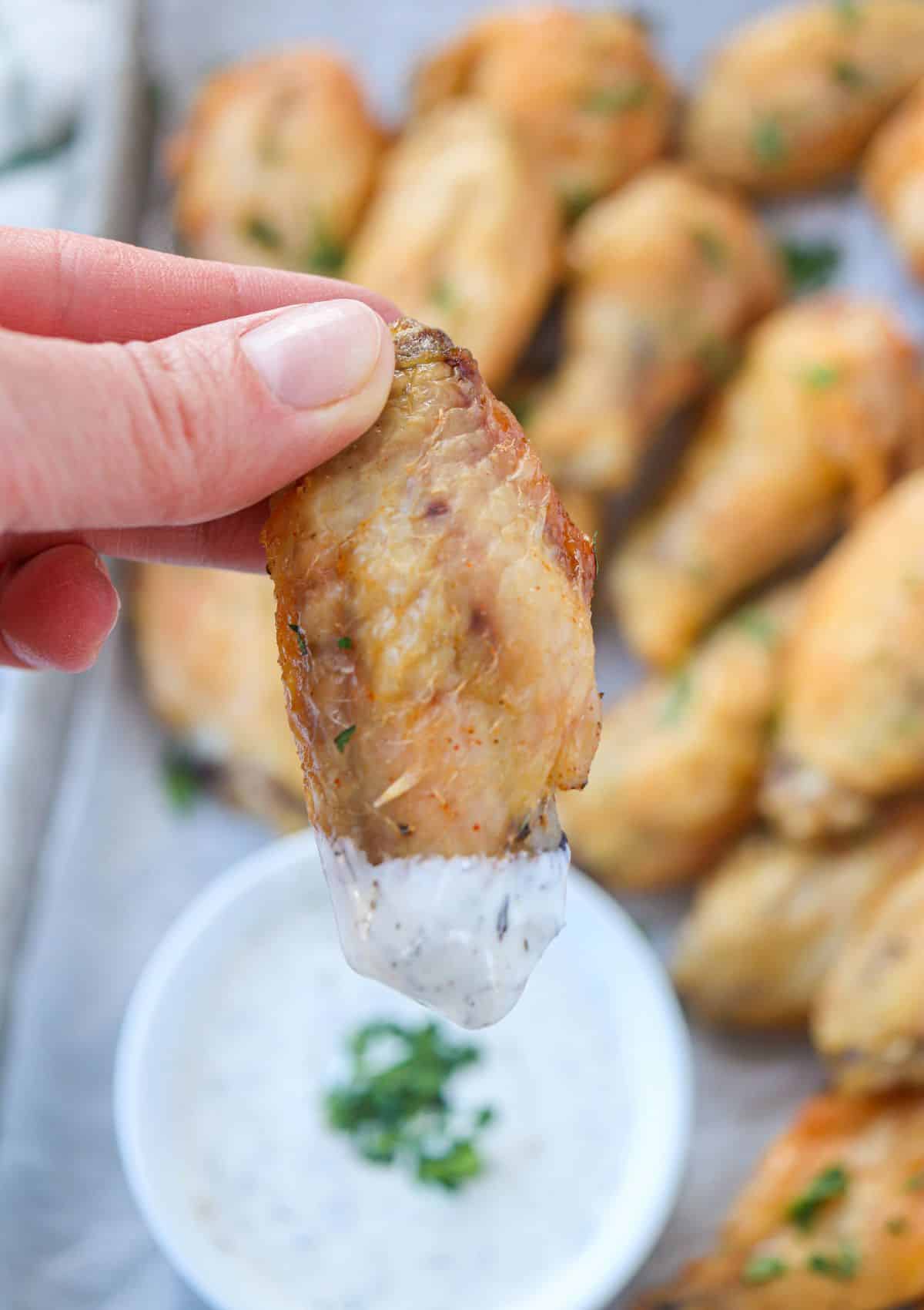 brined chicken wings browned and crispy stacked with a side of ranch dip, one wing is being dipped.