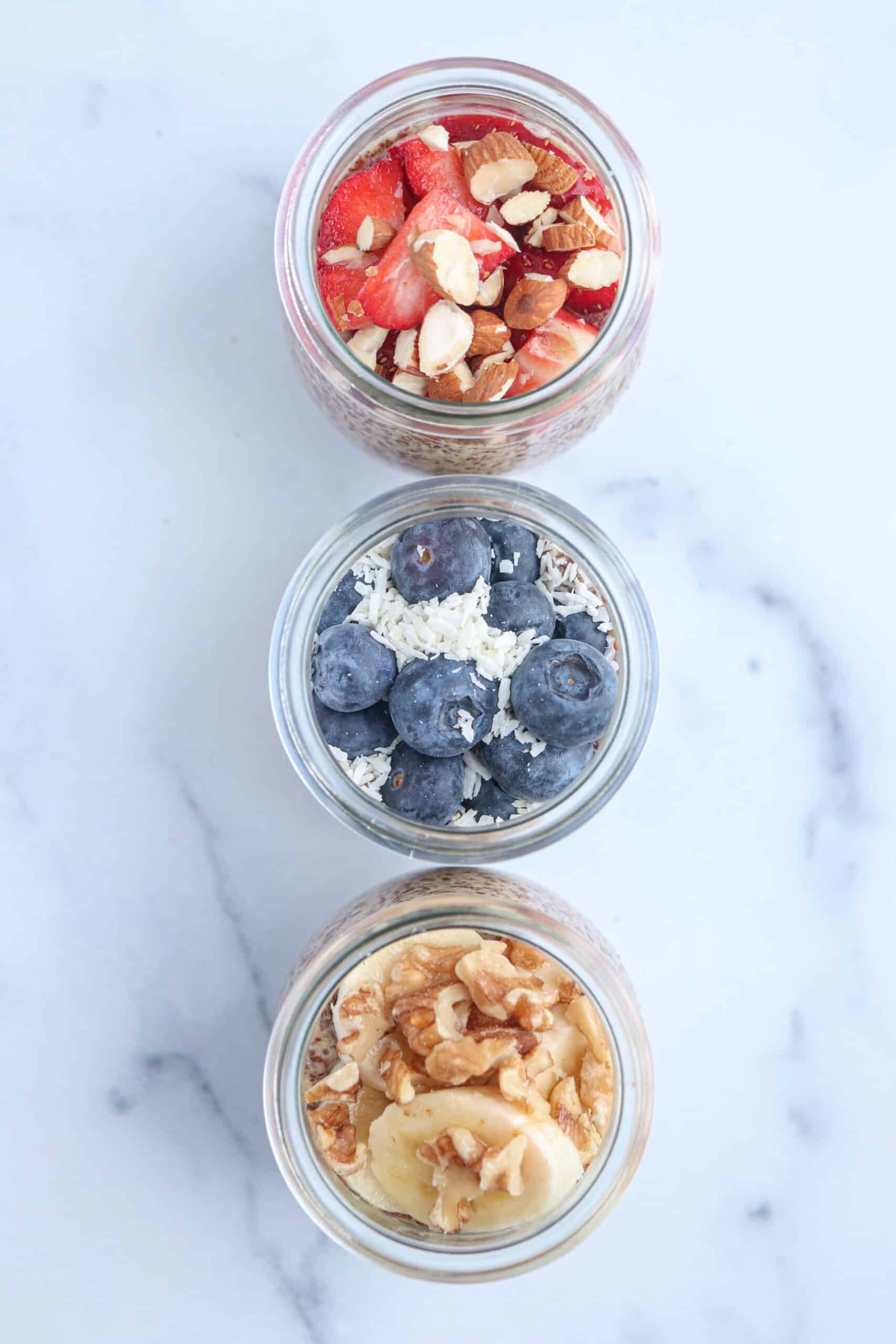 three small jars of flaxseed pudding topped with fresh fruit, nuts and coconut, overhead shot.