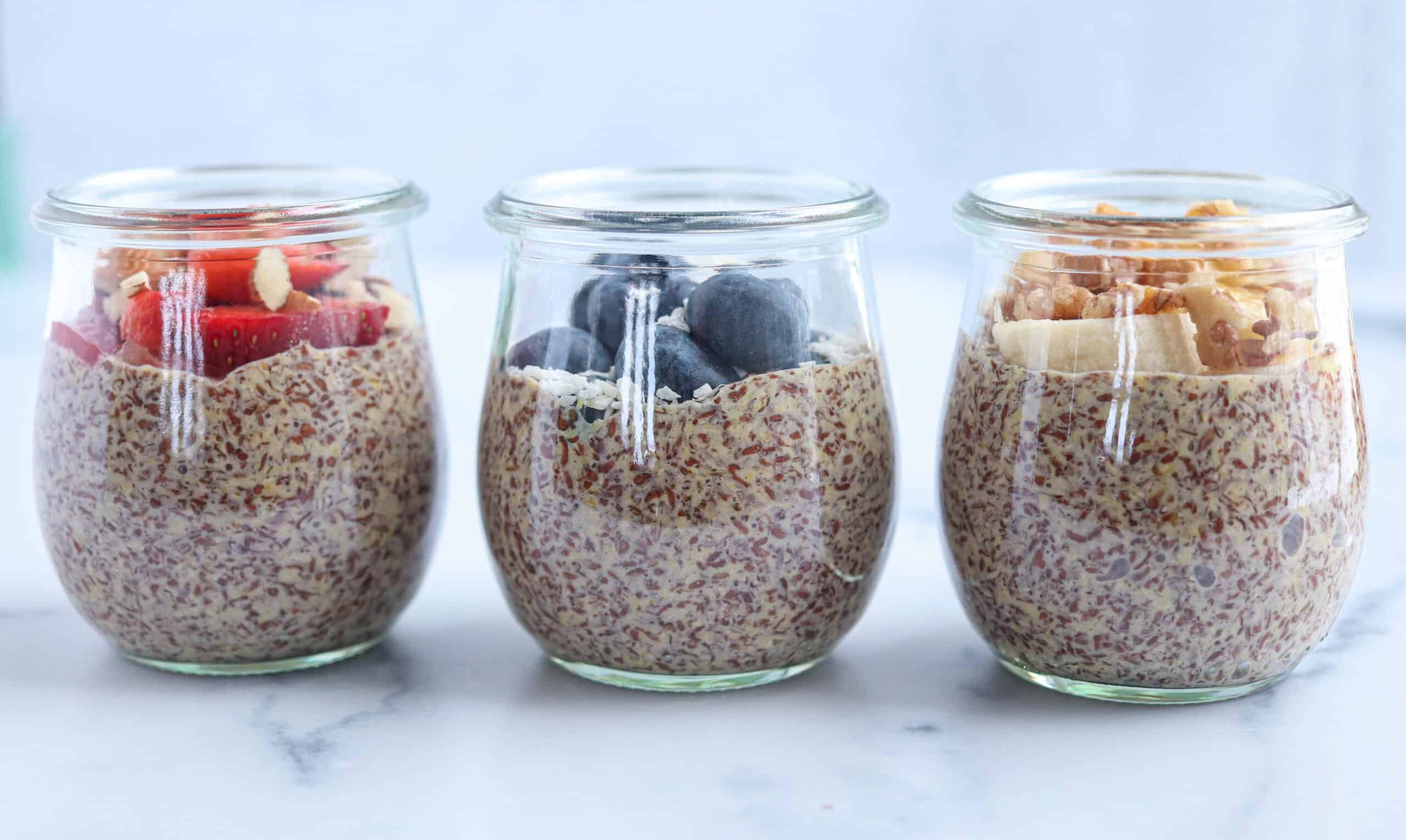 three small jars of flaxseed pudding topped with fresh fruit, nuts and coconut.
