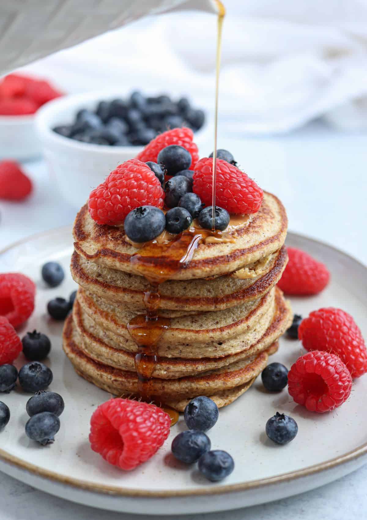 a stack of five protein banana oatmeal pancakes topped with fresh berries and maple syrup on a gray plate.