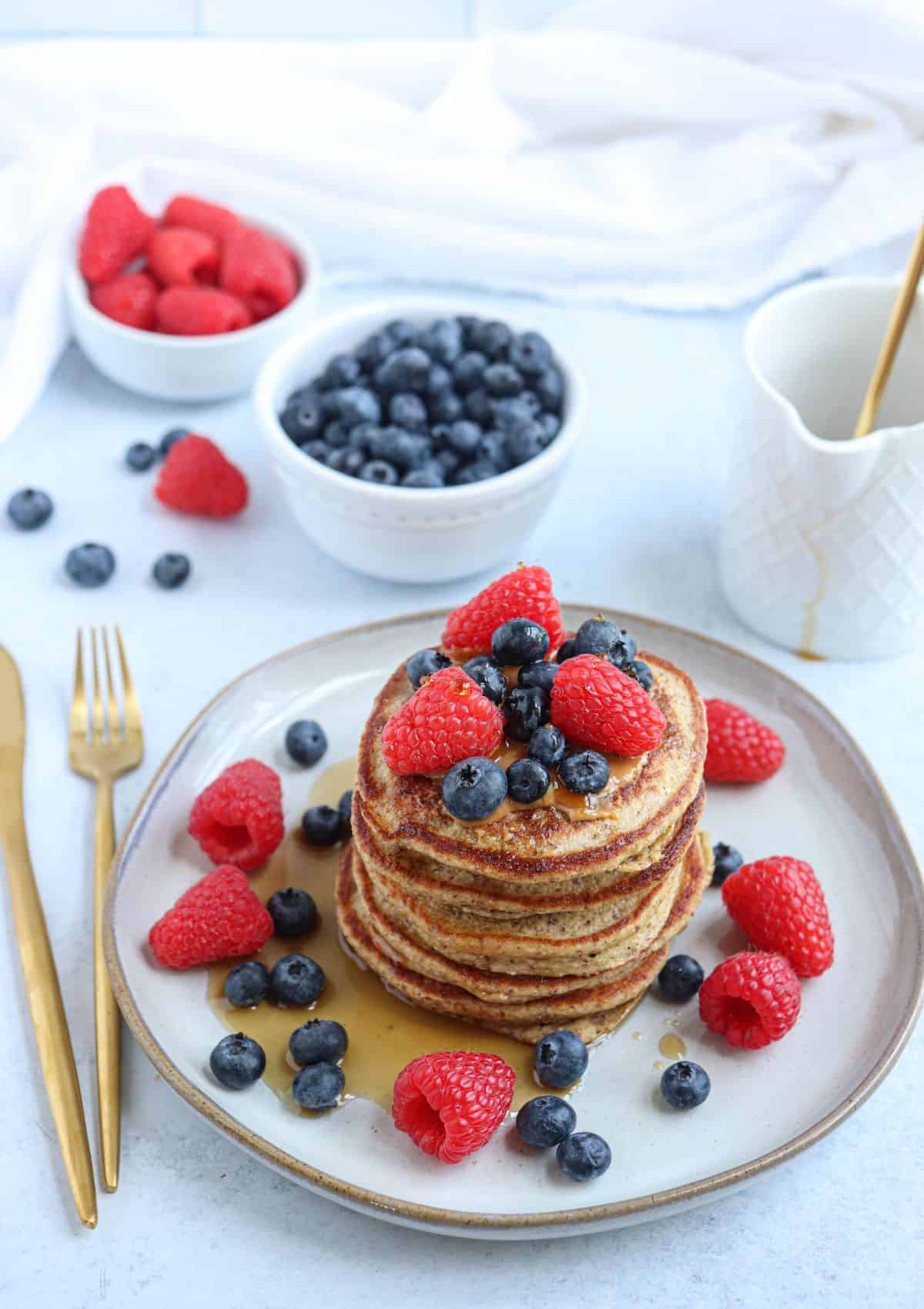 a stack of five protein banana oatmeal pancakes topped with fresh berries and  maple syrup on a gray plate.