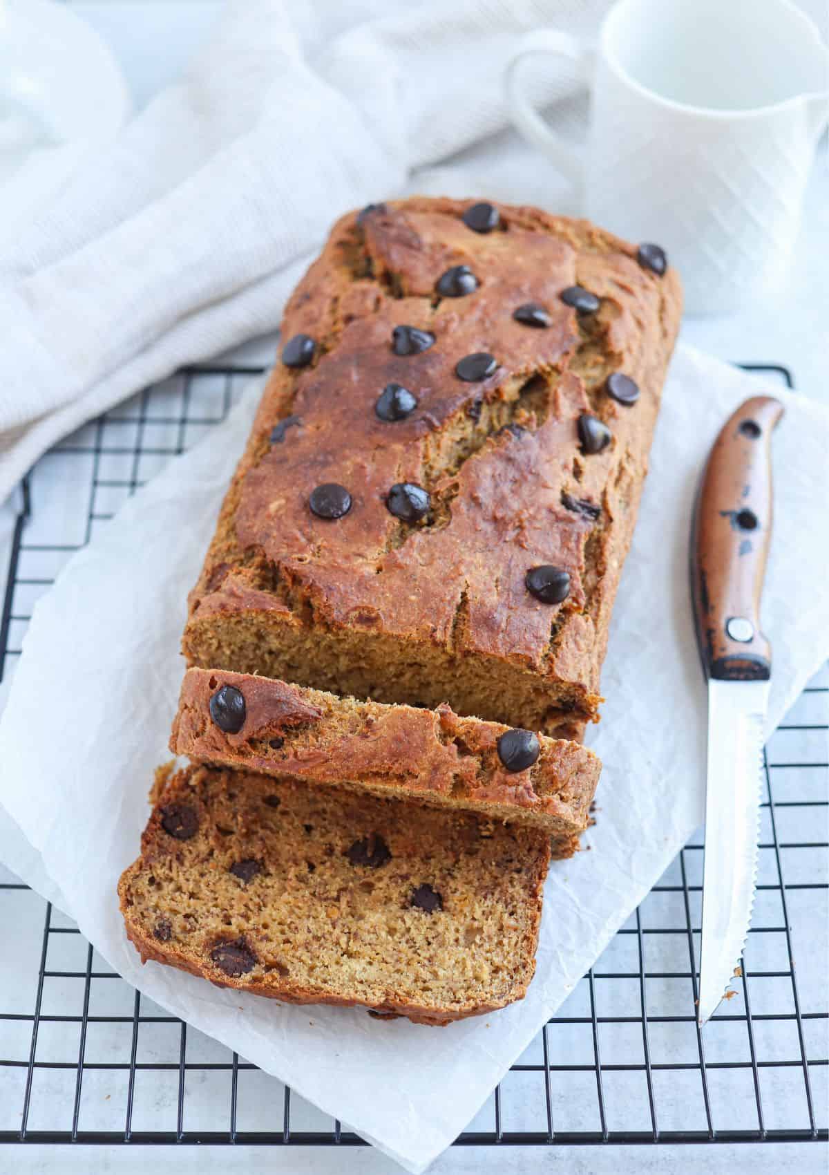 sweet potato banana bread with chocolate chips on parchment paper on a black wire rack, 2 slices are cut.