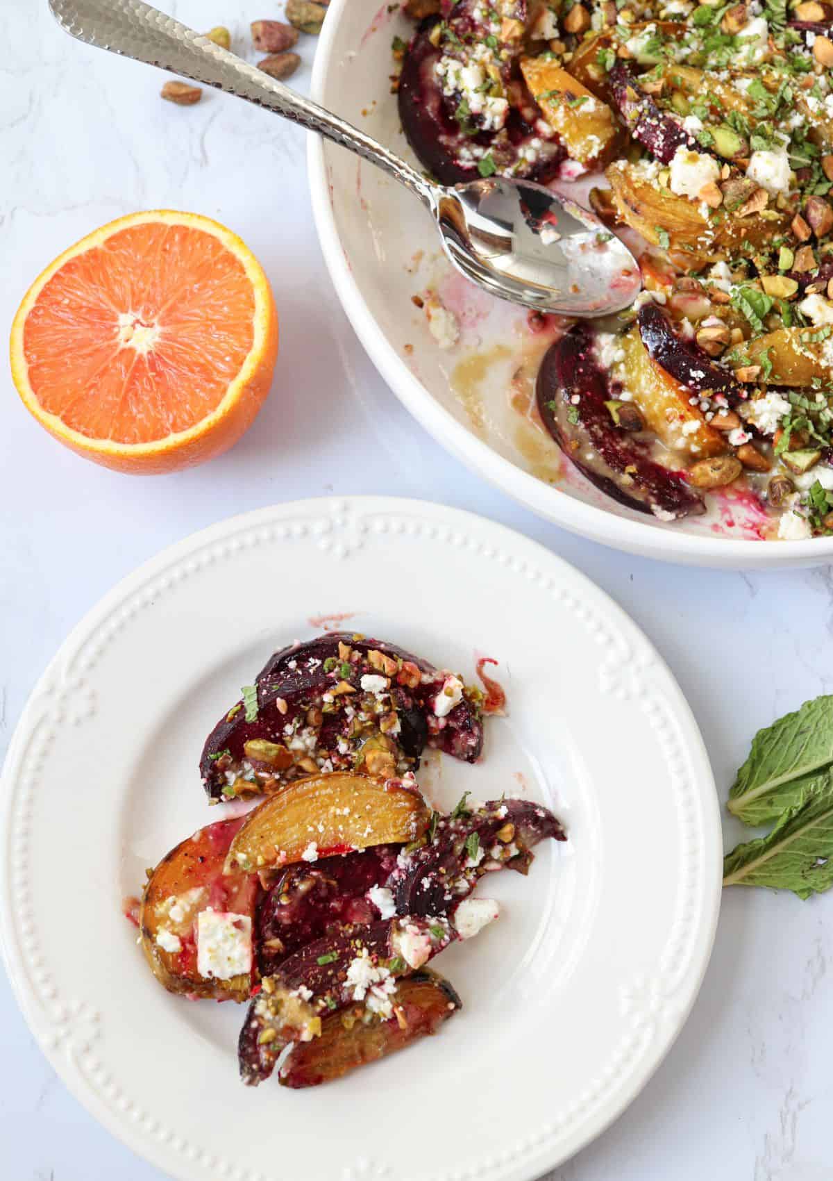 roasted beet salad with feta, tahini orange dressing, pistachios and chopped mint on a small white salad.