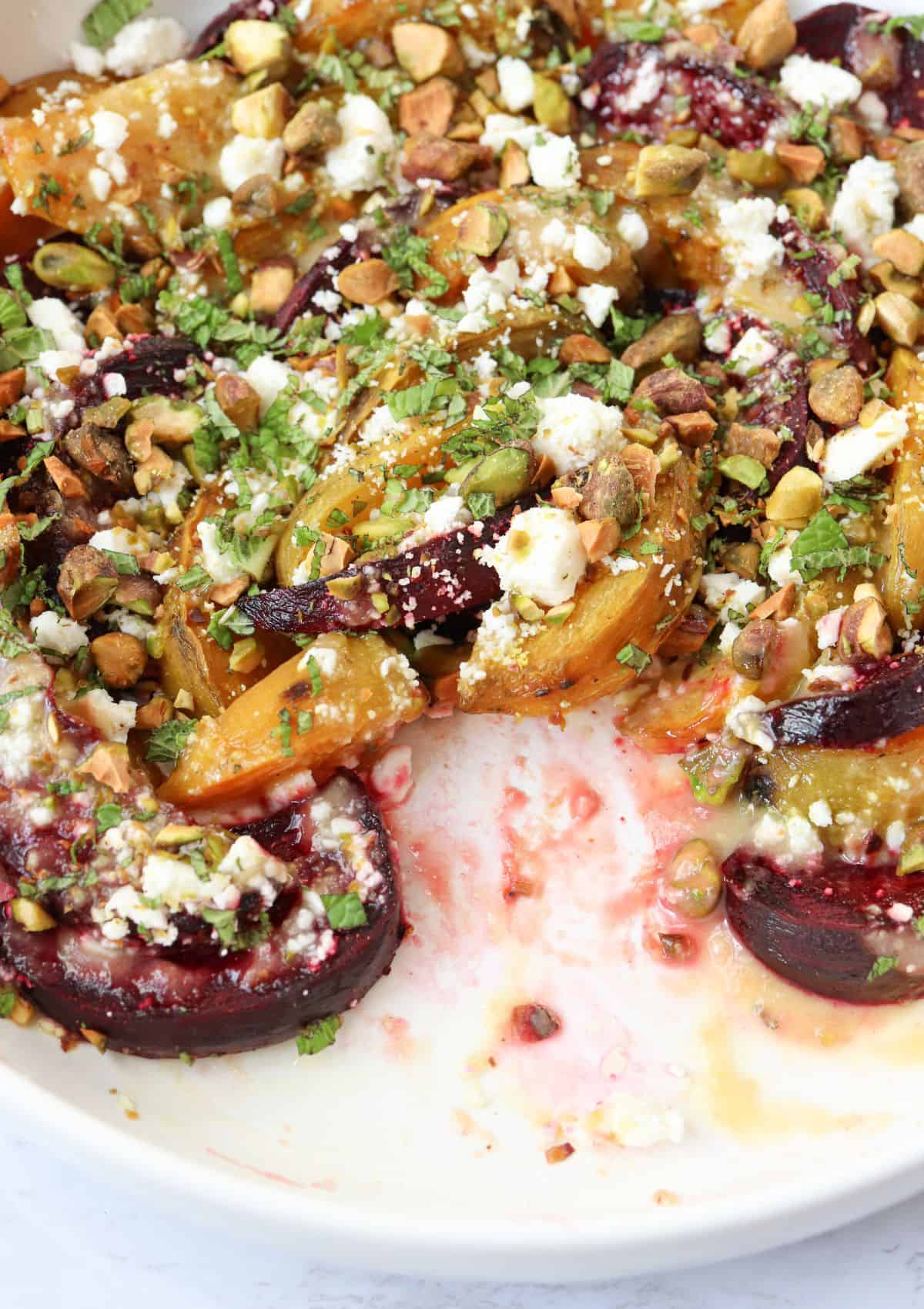 roasted beet salad with feta, tahini orange dressing, pistachios and chopped mint in a round white dish.