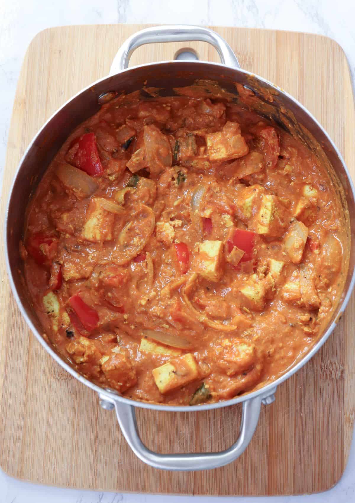 Indian tofu curry in a steel shallow saucepan on a bamboo board.