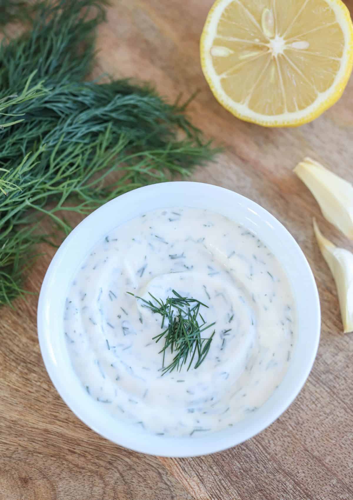 dill aioli in a small white bowl on a wooden board.