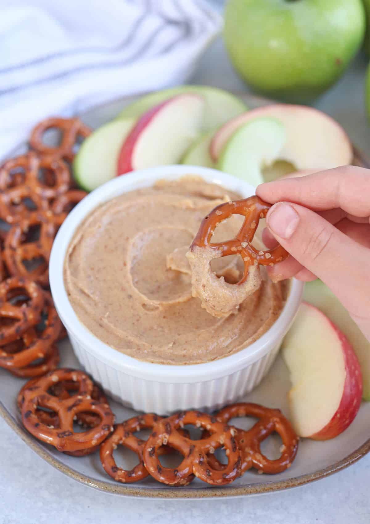 healthy yogurt caramel dip in a white ramekin with a hand dipping a small pretzel in.