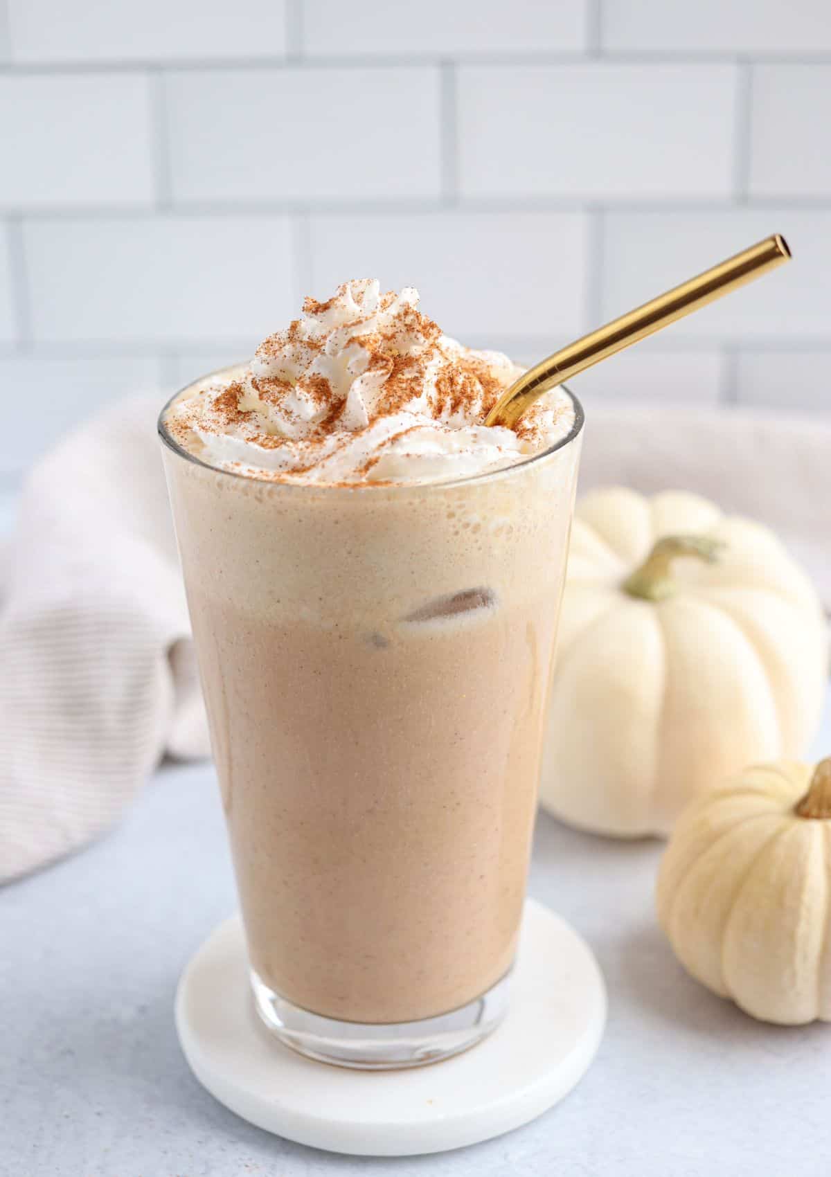 iced pumpkin spice latte in a pint glass with whipped cream and cinnamon on top and a golden straw.