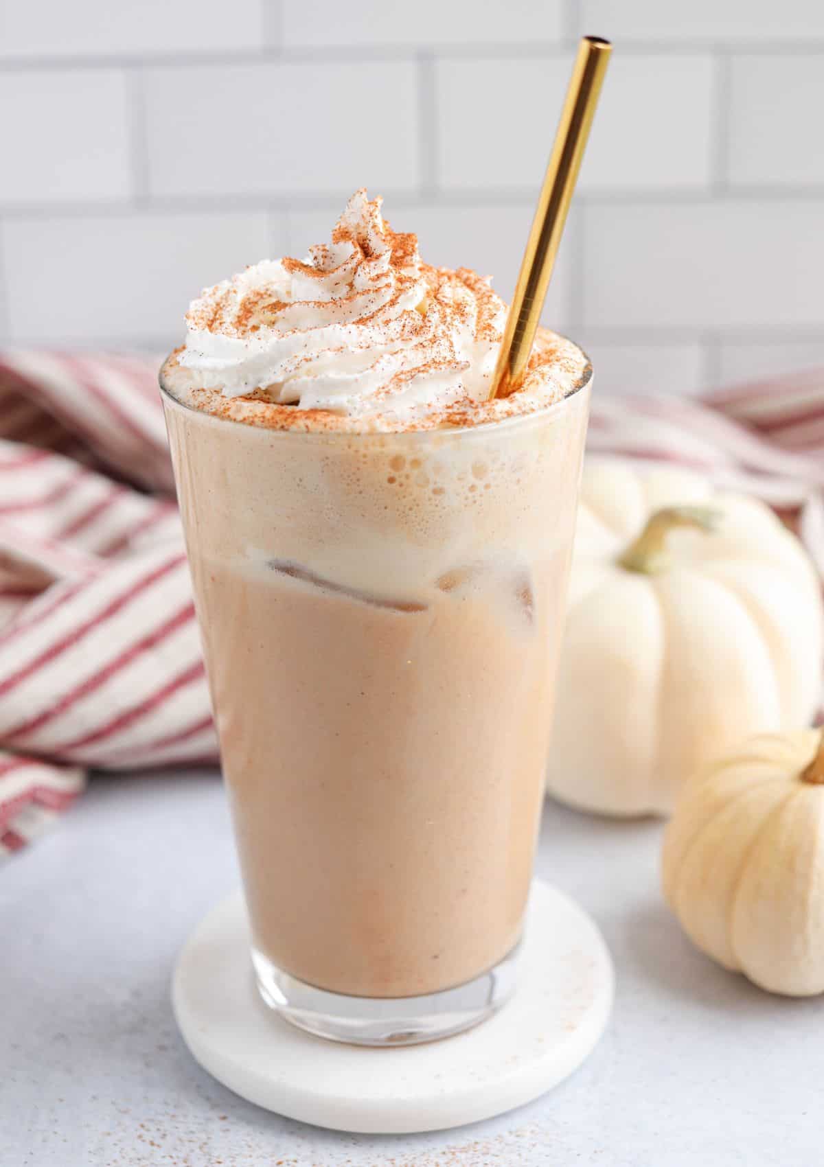 iced pumpkin spice latte in a pint glass with whipped cream and cinnamon on top and a golden straw.