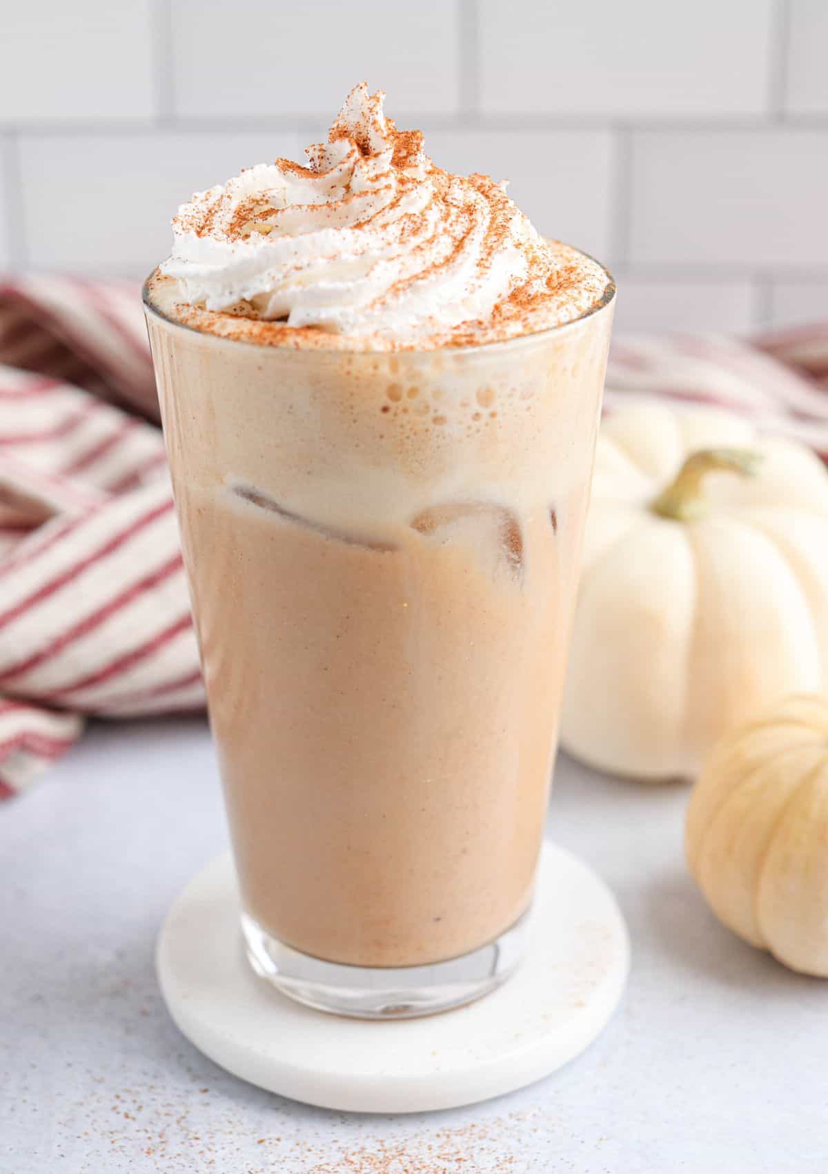 iced pumpkin spice latte in a pint glass with whipped cream and cinnamon on top.