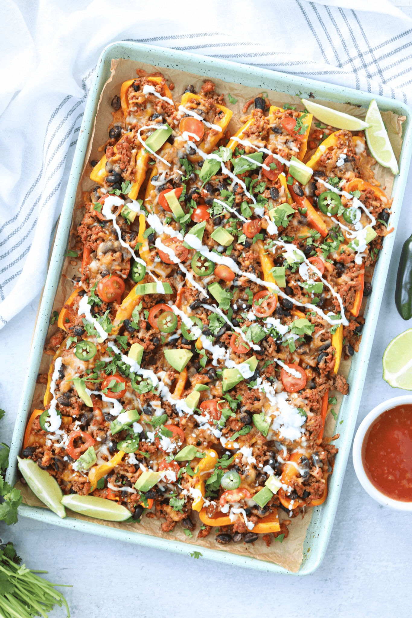 mini pepper nachos with ground meat, avocado and garnishes on teal baking tray.