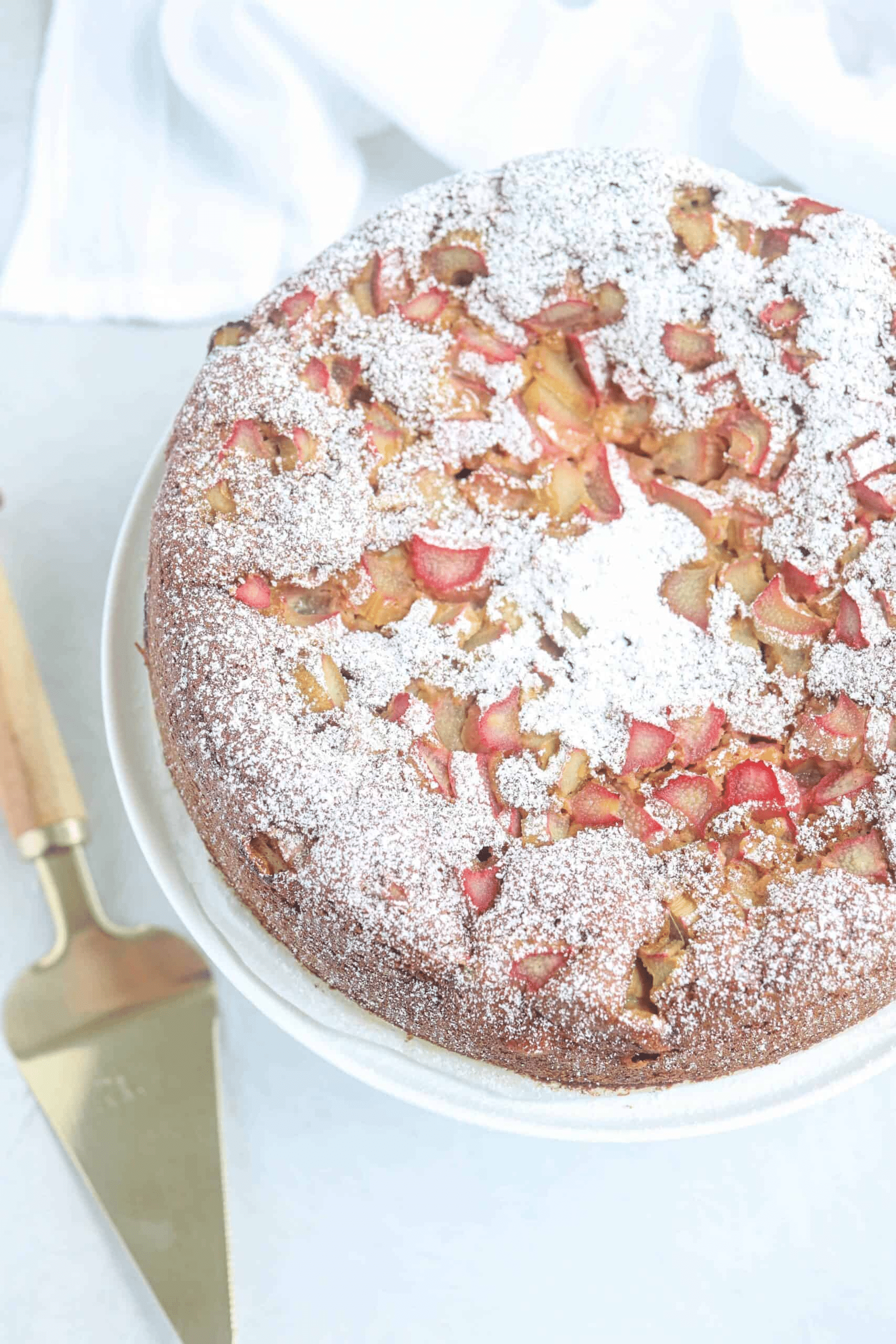 rhubarb cake dusted with powdered sugar on a white stand, overhead view. 