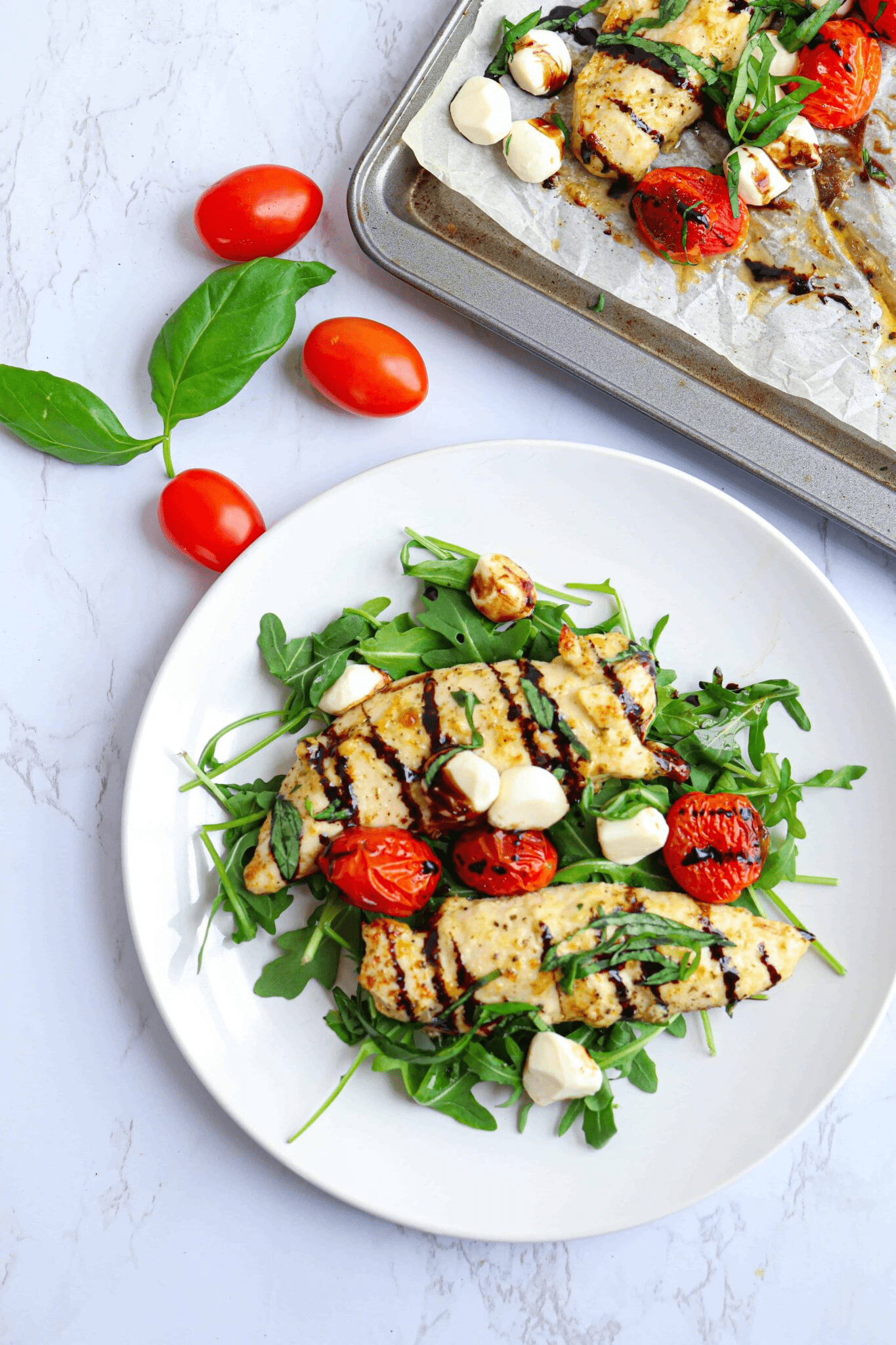 chicken tenders with mozzarella mini balls, roasted cherry tomatoes, fresh basil and balsamic drizzle on a white plate.