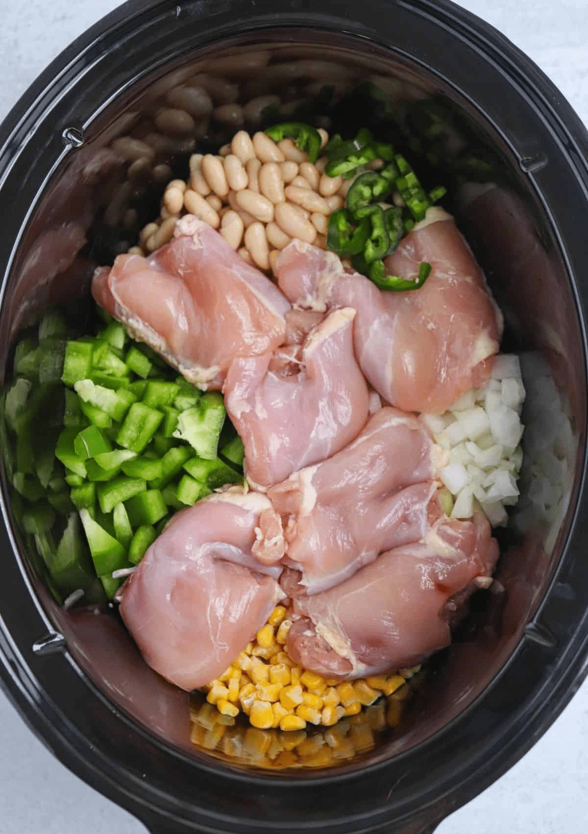 making green chicken chili in a black slow cooker, before cooking.