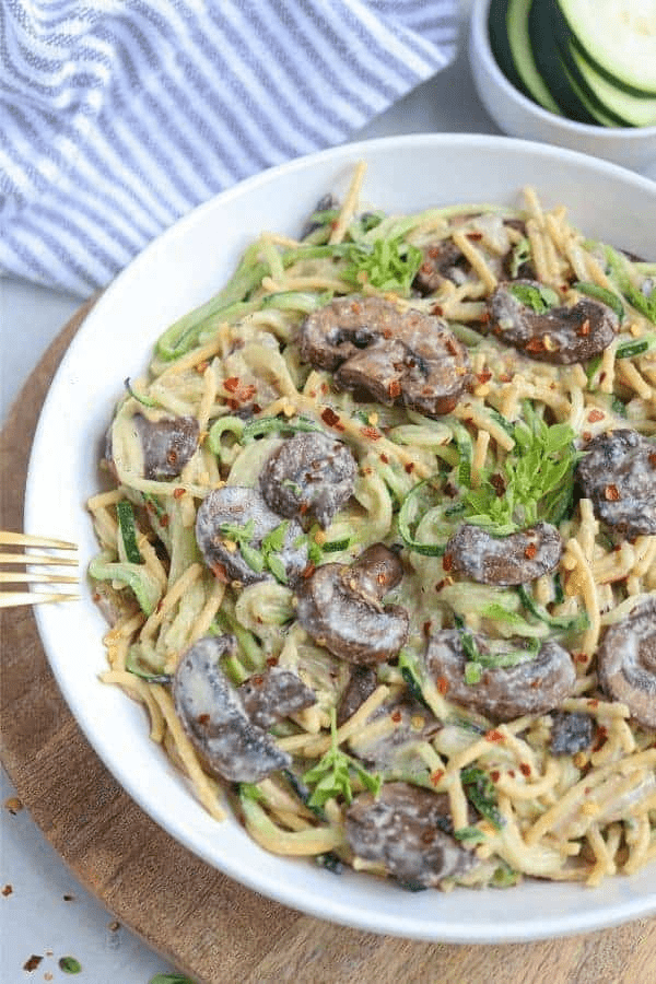 mushroom zucchini pasta in a white bowl on a wooden board.