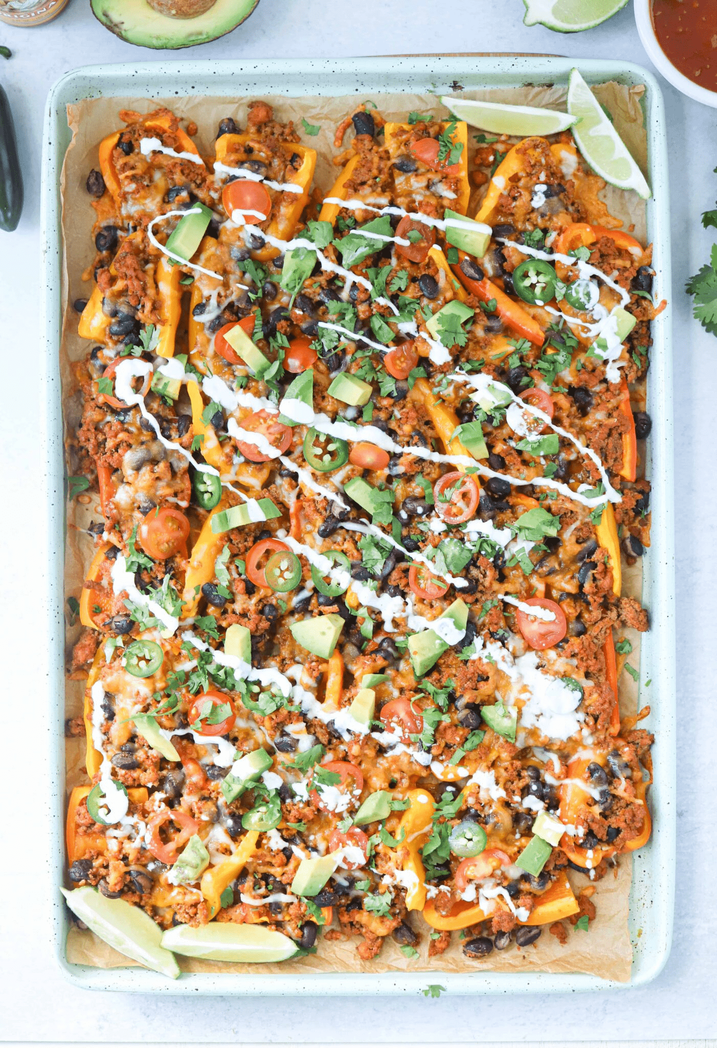 mini pepper nachos with ground meat, avocado and garnishes on teal baking tray.