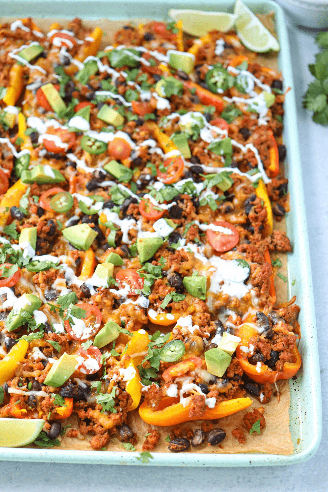 mini pepper nachos with ground meat, avocado and garnishes on teal baking tray.