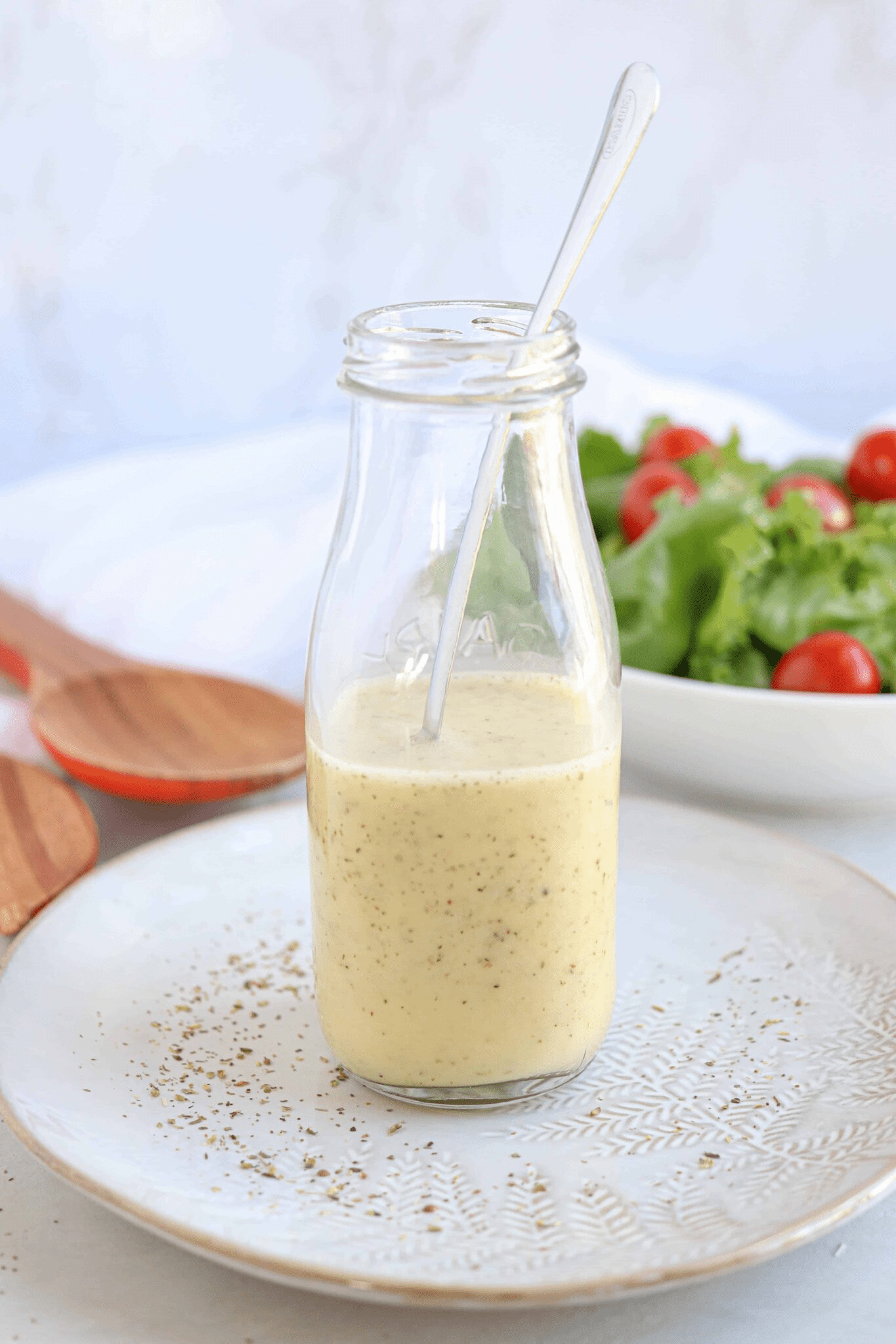 Greek salad dressing in a glass bottle with a spoon inside on a gray plate.