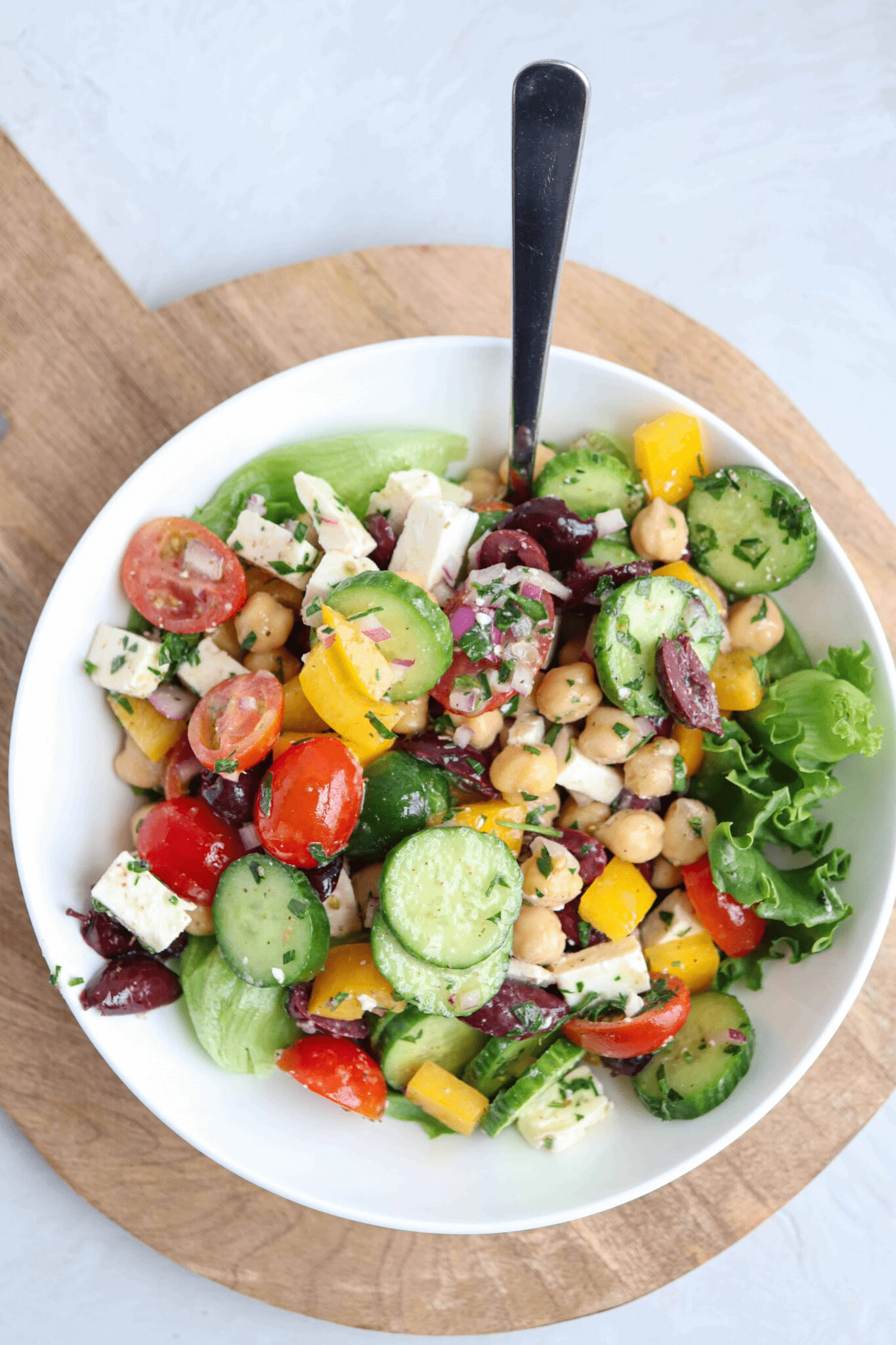 Greek chickpea salad with feta cheese, tomatoes, cucumbers and chickpeas in a white bowl.